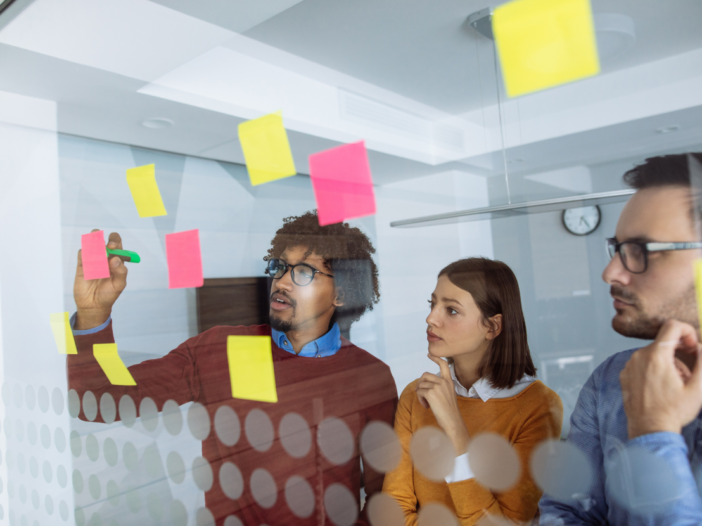 Three people - two men and a woman, white skin and brown skin working together on a problem in an office to illustrate why is diversity and inclusion important in the workplace