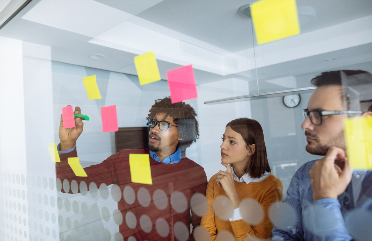 Three people - two men and a woman, white skin and brown skin working together on a problem in an office to illustrate why is diversity and inclusion important in the workplace