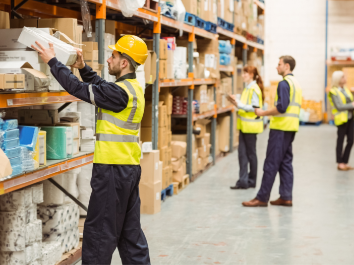 Workers in PPE stacking shelves in a warehouse to symbolise warehouse health and safety guidance.