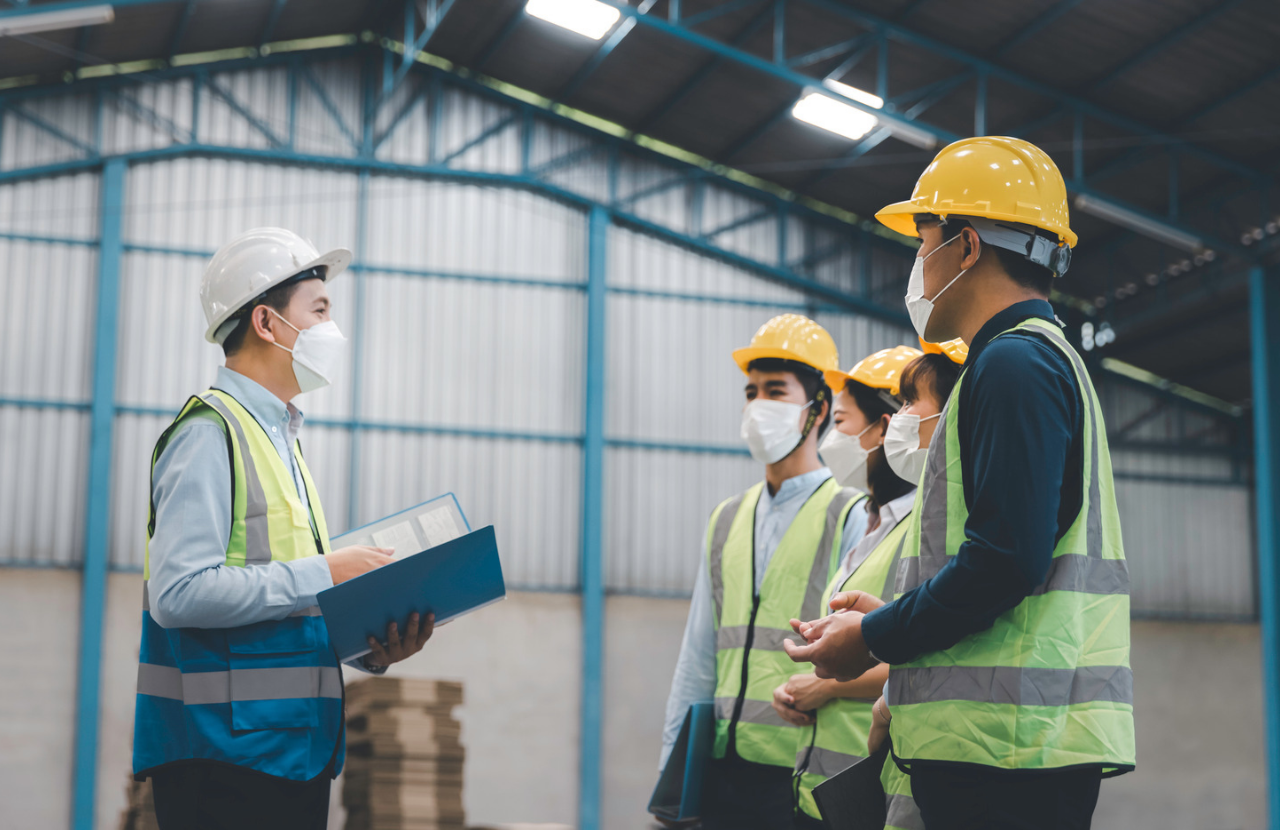 HSE investigation being carried out in a warehouse with four people in PPE and one holding a clipboard.